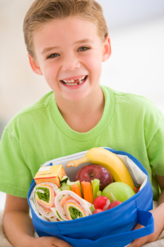 Young boy holding packed lunch in living room smiling