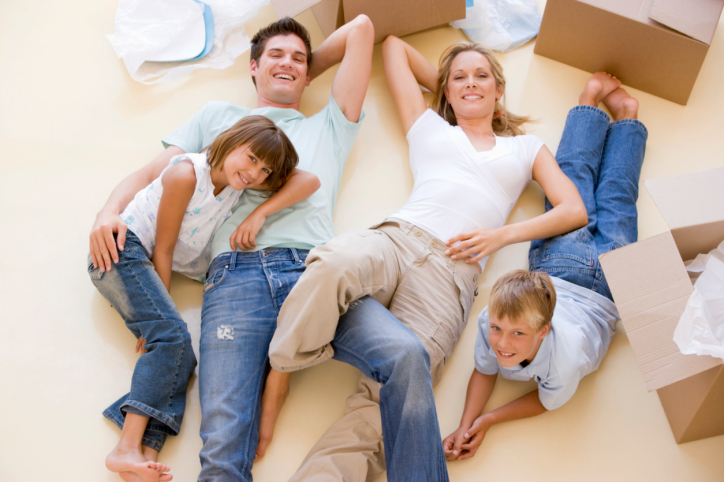 Family lying on floor by open boxes in new home smiling